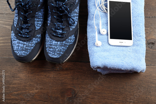 Sport shoes, towel and smart phone on wooden background