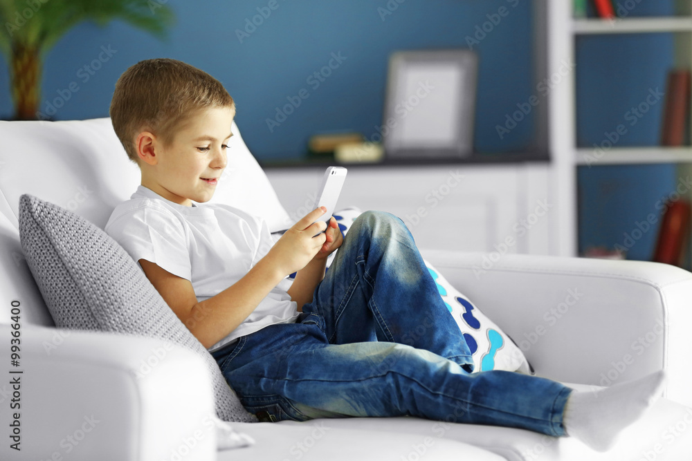 Little boy with mobile phone sitting on a sofa at home Little boy with mobile phone sitting on a sofa at home