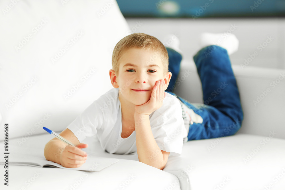 Little boy with notebook and pen on a sofa at home Little boy with notebook and pen on a sofa at home