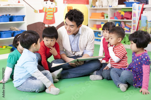 Male teacher reading picture book with cute kindergarten children