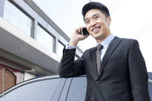 Cheerful businessman on the phone beside a car