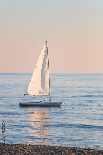 small sailboat in the water anchored next to the beach