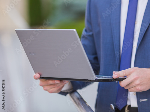 Successful businessman standing in the street holding a laptop