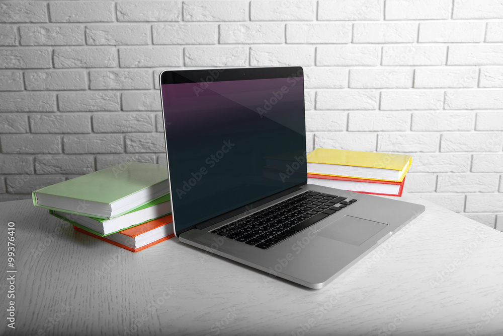 Laptop with books on brick wall background Laptop with books on brick wall background