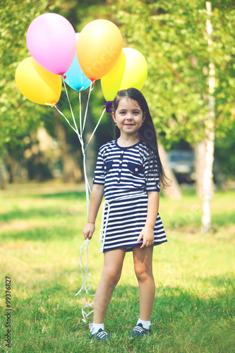 Happy little girl in striped dress with colourful balloons in the park