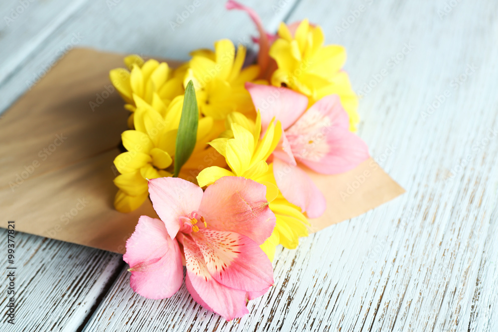 Pink alstroemeria and yellow chrysanthemum in envelope on wooden background Pink alstroemeria and yellow chrysanthemum in envelope on wooden background