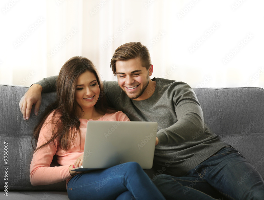 Young happy couple using laptop at home on light background