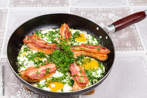 Delicious bacon strips, sausages and fried eggs breakfast in pan