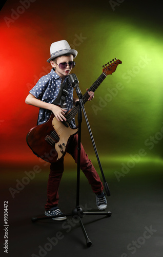Little boy playing guitar and singing with microphone on a bright background