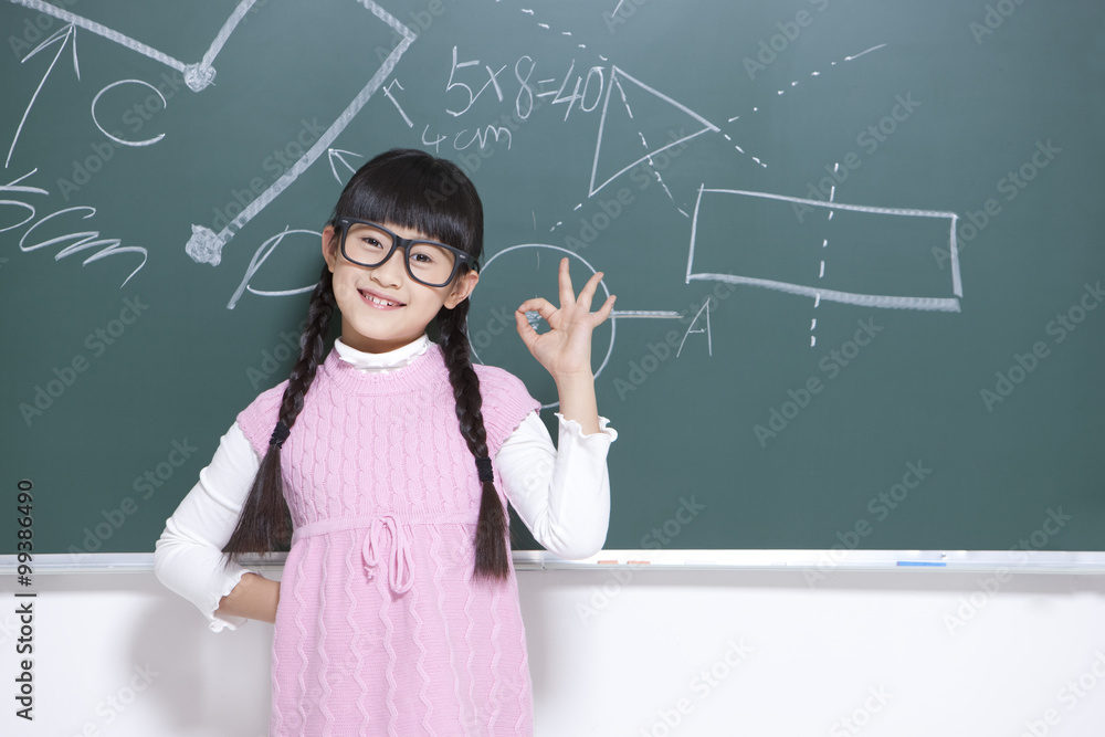 Cheerful little girl doing hand sign in classroom