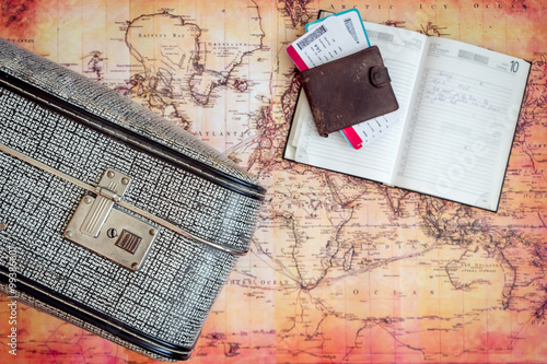 Suitcase, diary and tickets on old map background
