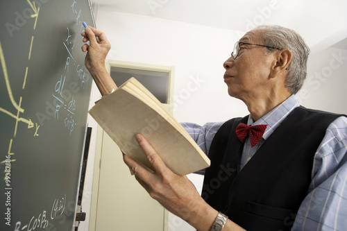 Teacher Holding Book And Writing On A Blackboard