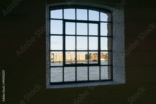 View framed by black surrounding wall to recent architectural buildings on other side River Thames through old wharf warehouse building windows from the dark interior at Wapping  London buildings 