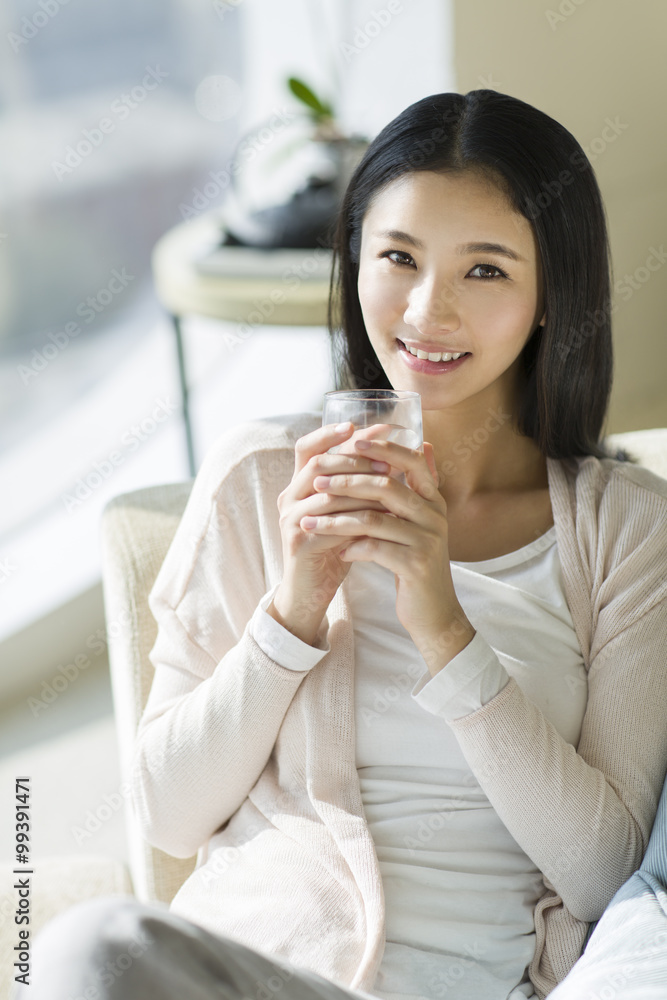 Happy young woman drinking water on sofa Happy young woman drinking water on sofa