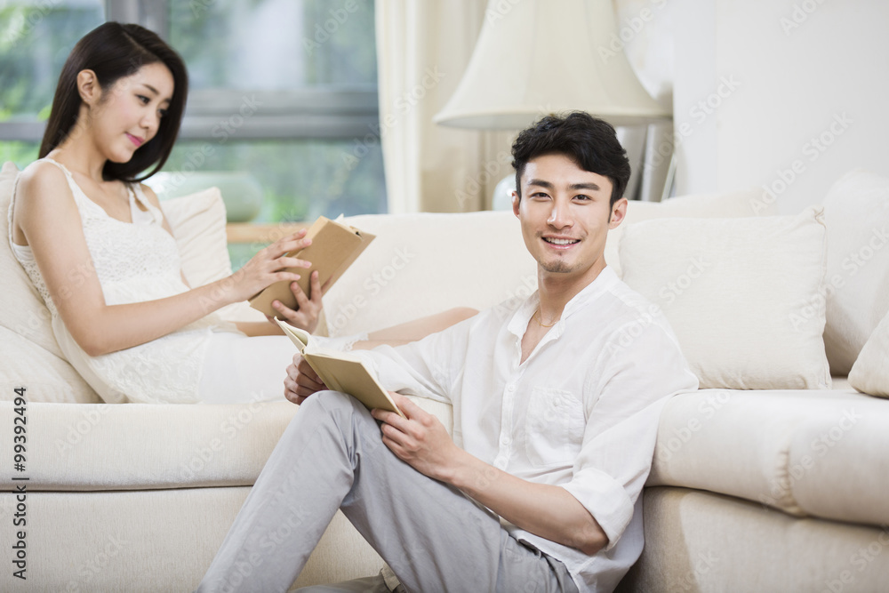 Cheerful young couple reading book in living room Cheerful young couple reading book in living room