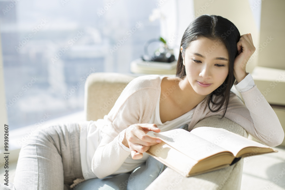 Happy young woman reading a book on sofa Happy young woman reading a book on sofa