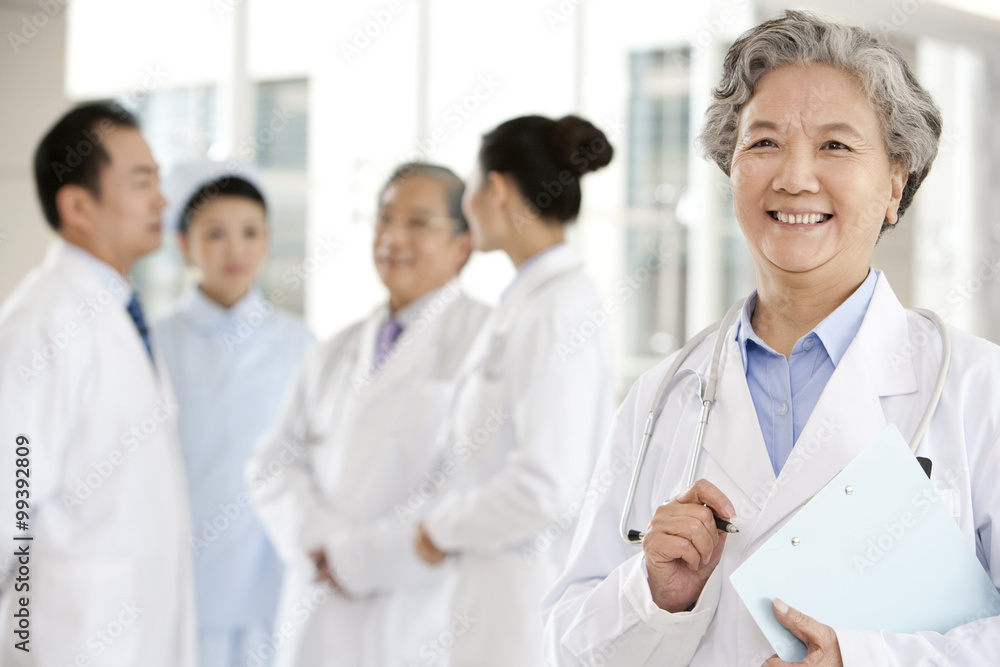 Senior Doctor in Forground with Clipboard, Doctors and a Nurse in Background