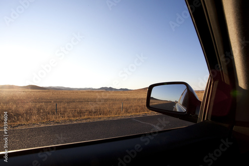Car sideview mirror with road going through field in the background