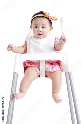Bild auf Leinwand Adorable baby girl with a spoon on baby high chair