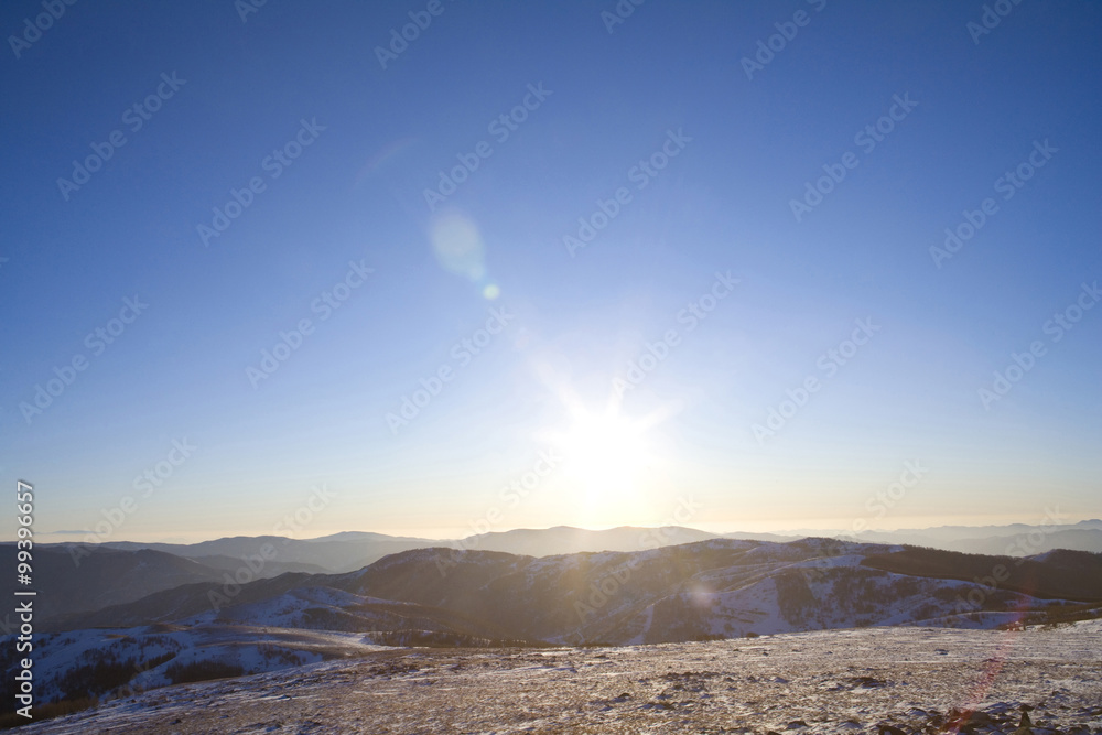 View of the sun setting over a mountain landscape View of the sun setting over a mountain landscape