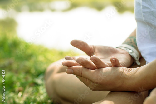 Closeup of female hands put in yoga mudra. Woman is meditating at the river-bank