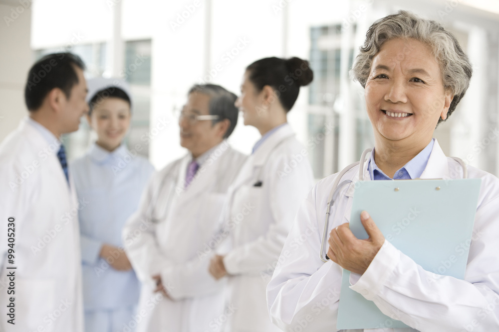 Senior Doctor in Forground with Clipboard, Doctors and a Nurse in Background Senior Doctor in Forground with Clipboard, Doctors and a Nurse in Background