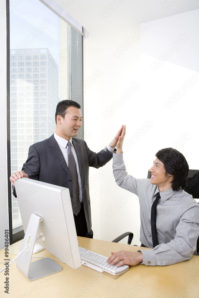 Man in business suit high-fives young employee who is using a computer Man in business suit high-fives young employee who is using a computer