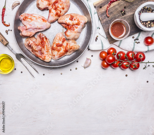raw chicken wings in barbecue sauce in the pan, with vegetables and spices on wooden rustic background top view close up