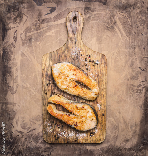 Two delicious grilled salmon steak with spices on a cutting board on wooden rustic background top view close up