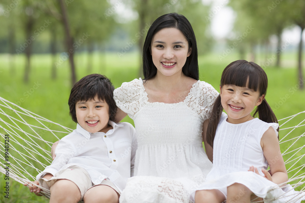 Happy young mother and kids sitting in a hammock outdoors Happy young mother and kids sitting in a hammock outdoors