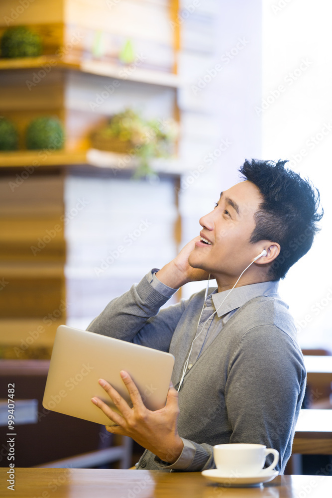 Young man enjoying music in digital tablet in coffee shop Young man enjoying music in digital tablet in coffee shop
