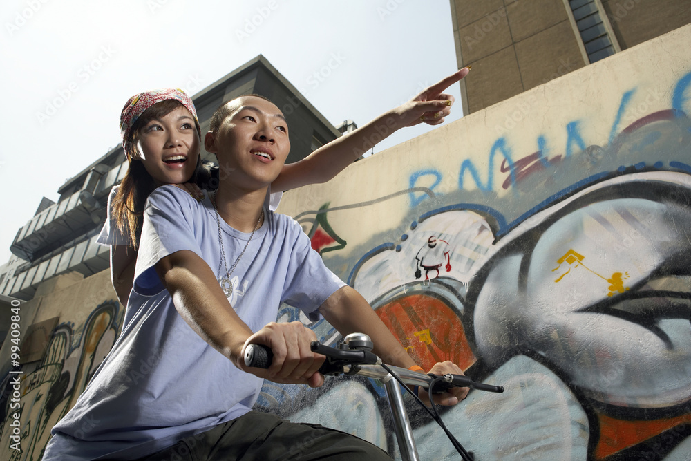 Obraz premium Teenage Boy And Girl On Bike In Front Of A Wall Of Graffiti