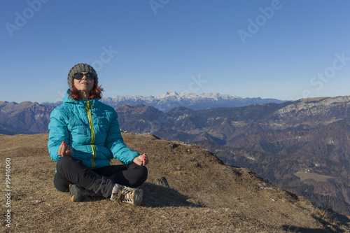 Pretty mid aged woman trekker relaxing, performing JOGA high in mountains on sunny winter day against  Mount Triglav, highest mountain in Slovenian  Alps, space for text