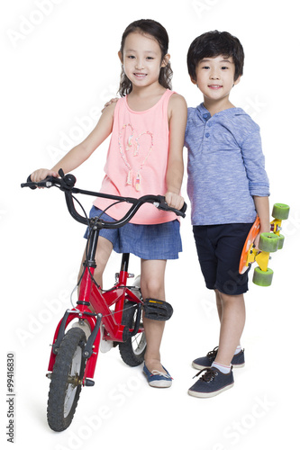 Little girl riding bike and boy holding a skateboard