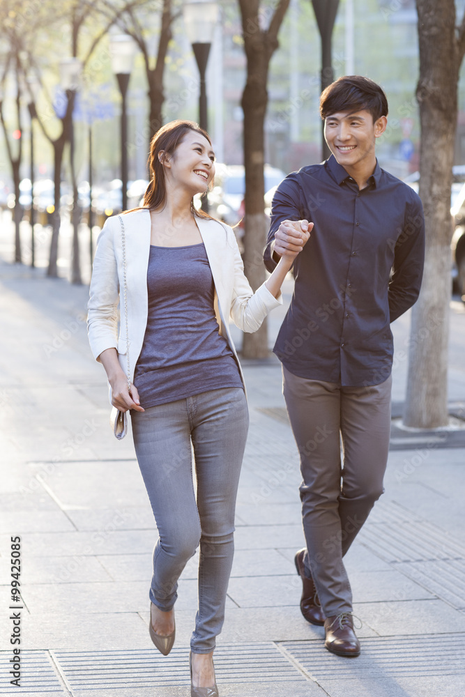 Young couple holding hands walking on sidewalk