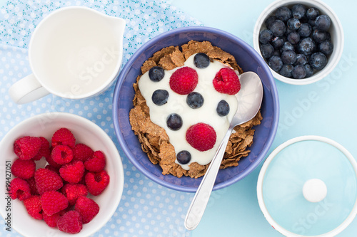 A breakfast table with bran flake cereal, raspberries, blueberries and natural yoghurt. A view from above. 