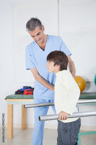 Male therapist with boy in parallel bars