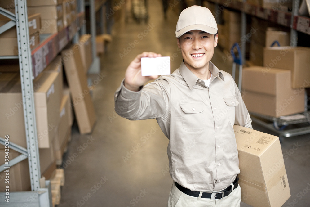 Male Chinese warehouse worker holding up a blank business card Male Chinese warehouse worker holding up a blank business card
