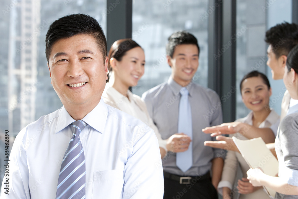 Businessman smiling with colleagues in the background Businessman smiling with colleagues in the background