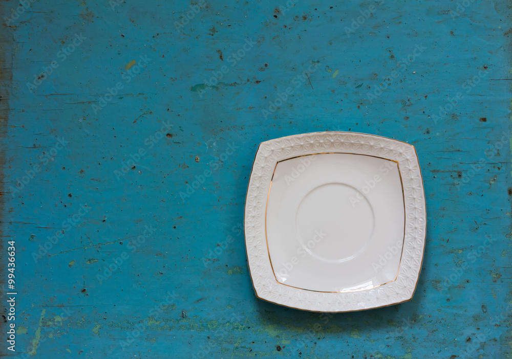 White ceramic square saucer on old blue wooden surface. Copy space. Free space for text. Close-up, top view White ceramic square saucer on old blue wooden surface. Copy space. Free space for text. Close-up, top view