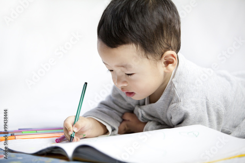 Happy little boy lying on front and writing