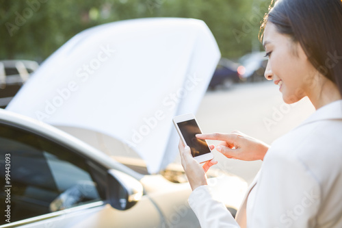 Female driver messaging on mobile phone next to broken down car photo