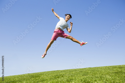 Cheerful young man jumping on grass