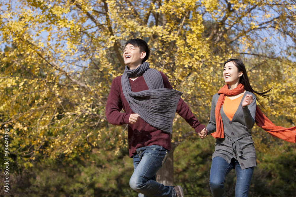 Cheerful young couple in love running on the lawn in autumn