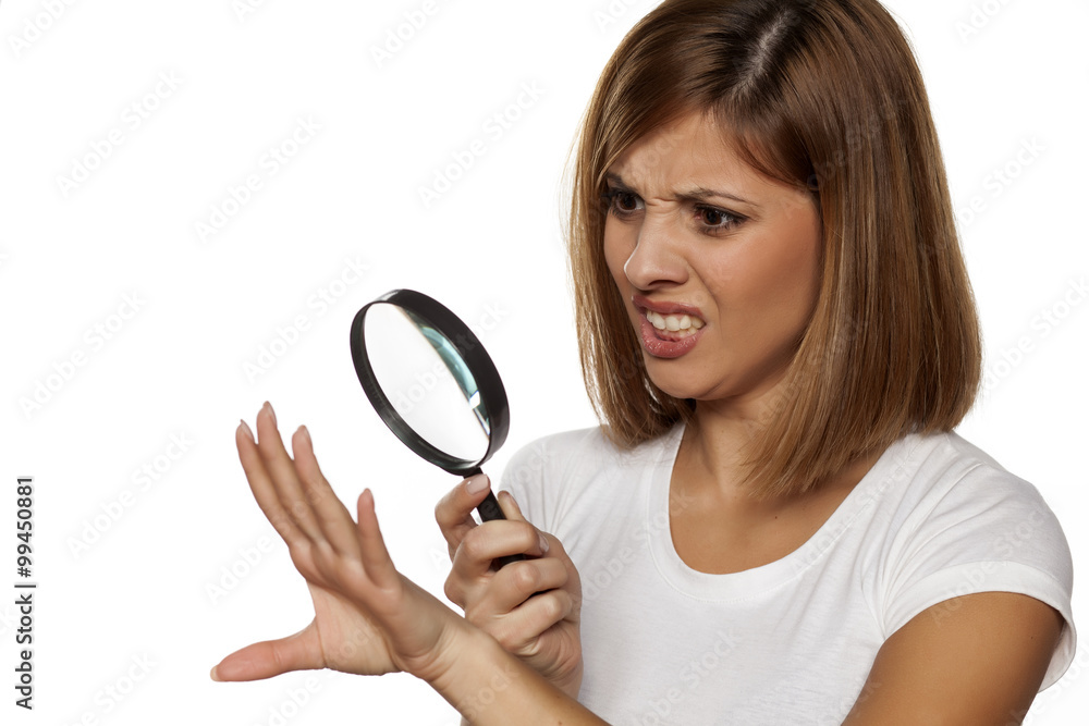 unhappy young woman analyze her nails with a magnifying glass unhappy young woman analyze her nails with a magnifying glass