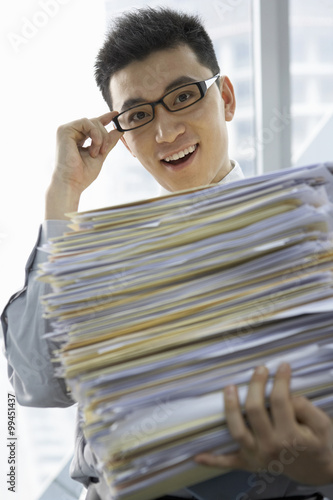 Businessman In Office Holding Pile Of Work