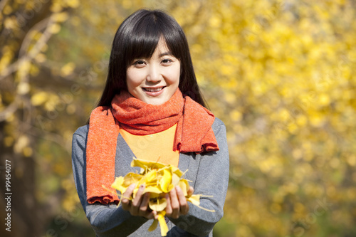 Smiling young woman holding autumn leaves outdoors