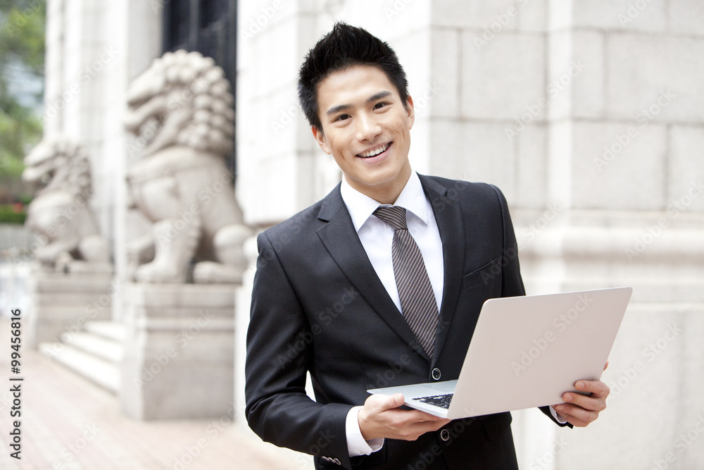 Cheerful young businessman with a laptop outside a building, Hong Kong