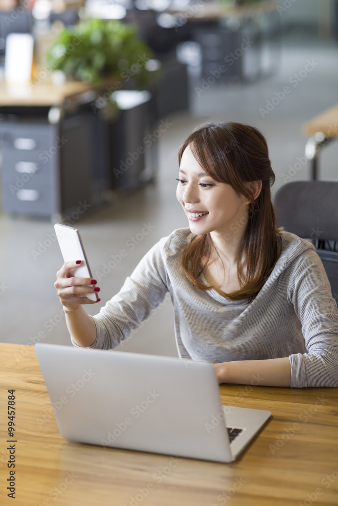 © Blue Jean Images - Young woman using smart phone in office