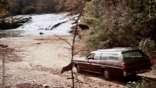 Station wagon driving on dirt road towards river
